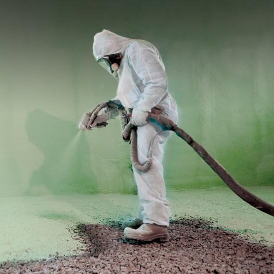 A worker covered head-to-toe in safety equipment coats surfaces in spray foam insulation.